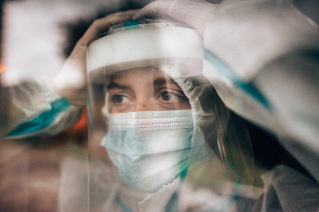 A close up of a doctor wearing PPE, including a mask, face shield, gloves, and hazmat suit.