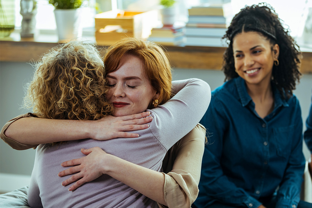Two women in a group counseling session embrace