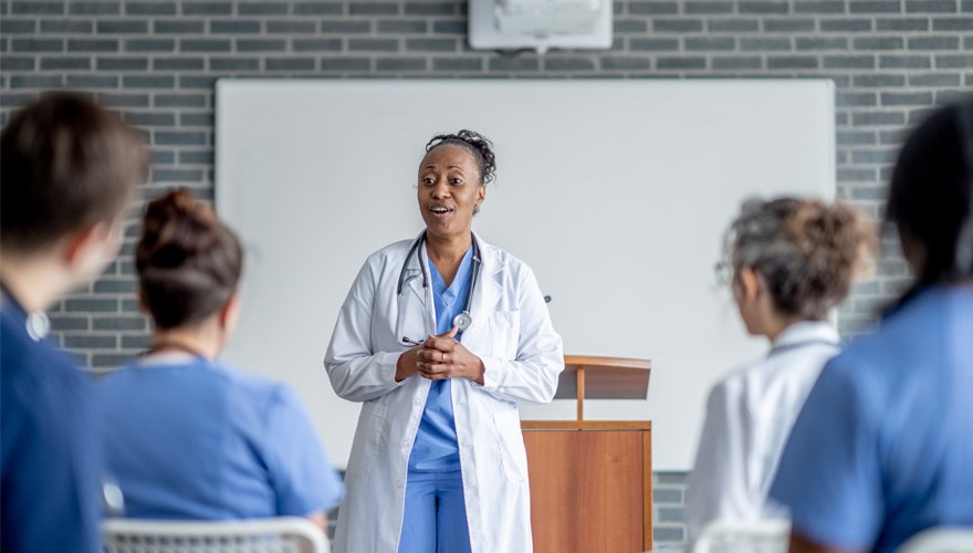 A black female doctor lectures at the front of a classroom. 