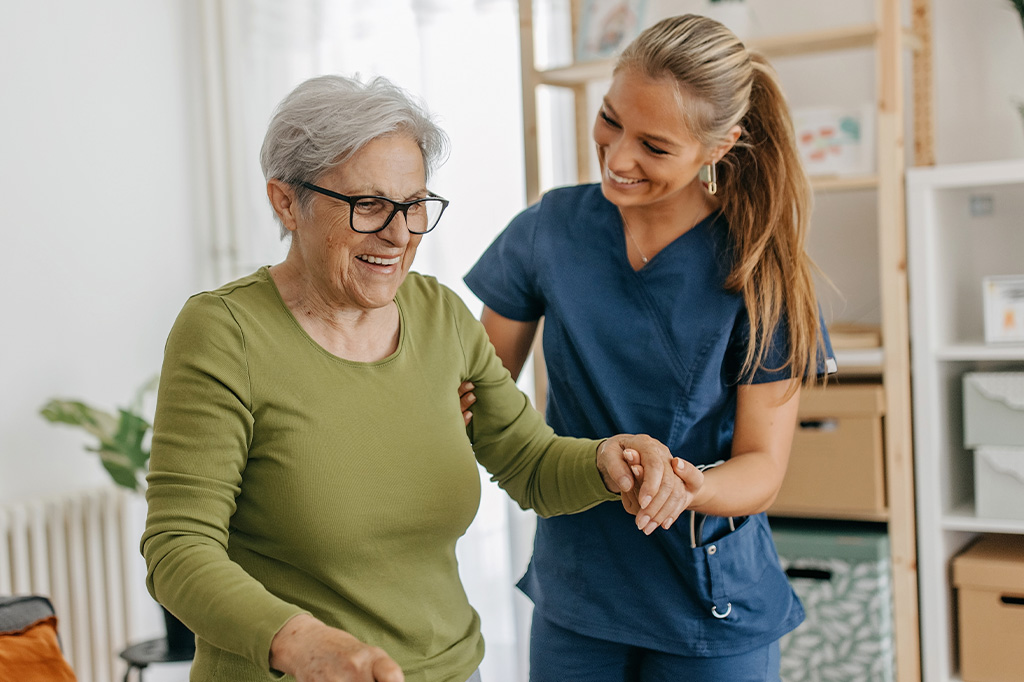 A nurse helps an elderly woman with a cane