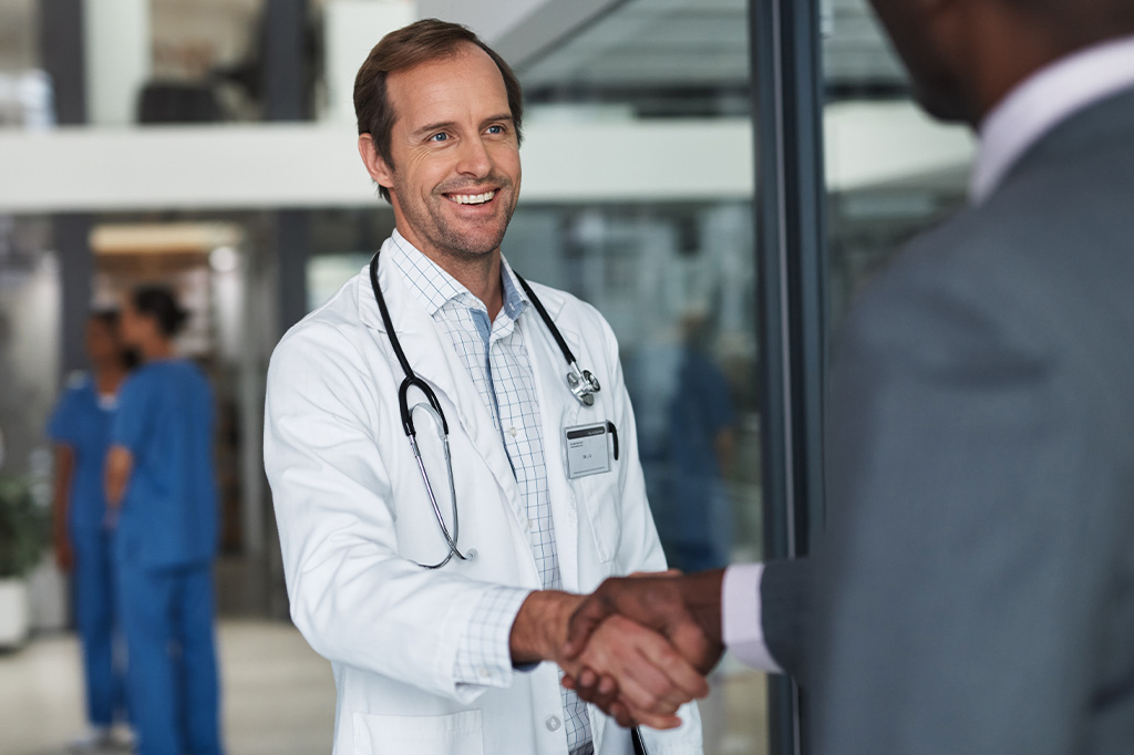 A doctor in white lab coat shakes hands with a man in business attire